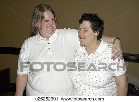 Stock Image - Two visually impaired women standing arm in arm, smiling in friendship.. Fotosearch