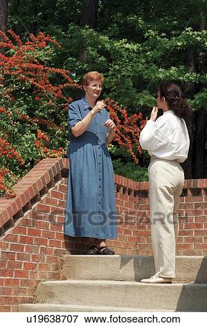 Stock Photo - Two women, both deaf or with hearing impairments, conversing via sign language outside a building following a seminar.. Fotosearch
