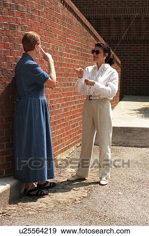 Stock Photo - Two women, both deaf or with hearing impairments, conversing via sign language outside a building following a seminar.. Fotosearch