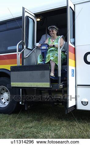 Stock Photograph - Woman with a disability, utilizing a scooter for assistance, disembarking from an accessible public transit bus.. Fotosearch