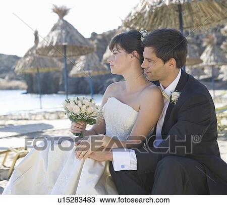 Stock Image - A bride and groom sitting on a beach. Fotosearch