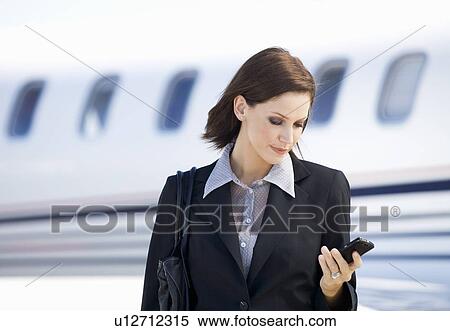 Stock Photography - A business woman talking on a mobile phone next to a plane. Fotosearch