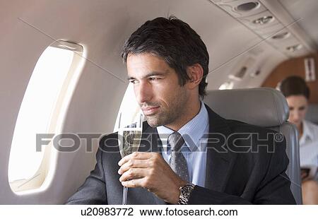 Stock Image - A businessman drinking champagne on a flight. Fotosearch