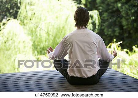 Stock Image - A businessman meditating in a garden. Fotosearch