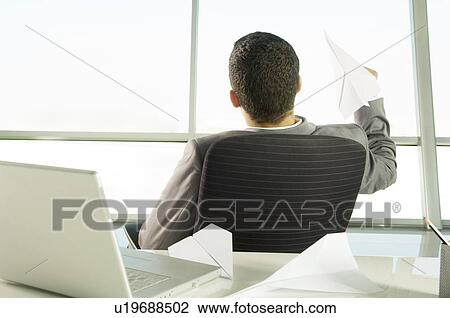 A businessman sitting at a desk making paper airplanes View Large Photo Image Stock Image - A businessman sitting at a desk making paper airplanes. Fotosearch