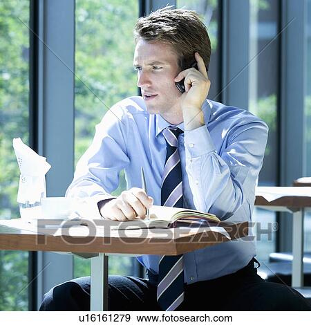 Stock Photo - A businessman talking on a mobile phone whilst waiting to travel. Fotosearch