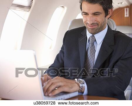 Stock Photo - A businessman using a laptop in a plane. Fotosearch