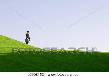 Picture - A businessman with a suitcase walking down hill. Fotosearch