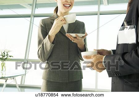 Picture - A businesswoman having a cup of coffee with a visiting colleague. Fotosearch
