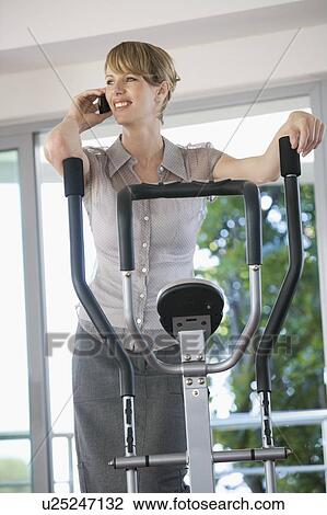 Stock Image - A businesswoman in a gym using a mobile phone. Fotosearch