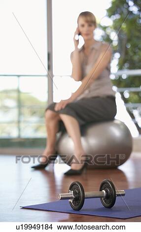 Picture - A businesswoman sitting in a gym using a mobile phone. Fotosearch