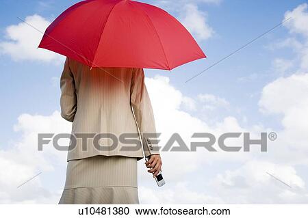 A businesswoman standing underneath an umbrella holding a mobile phone View Large Photo Image Stock Image - A businesswoman standing underneath an umbrella holding a mobile phone. Fotosearch