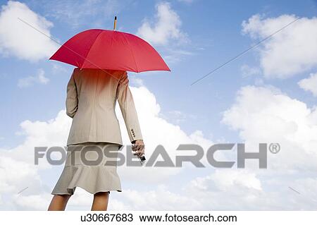 Stock Image - A businesswoman standing underneath an umbrella holding a mobile phone. Fotosearch