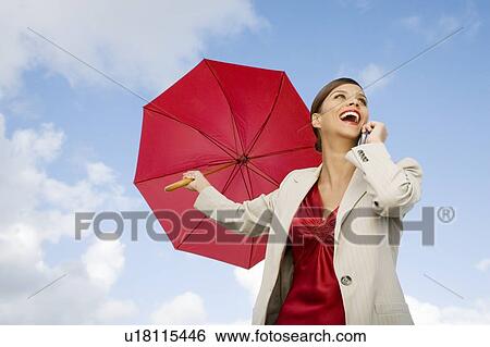 Stock Photograph - A businesswoman standing underneath an umbrella holding a mobile phone. Fotosearch