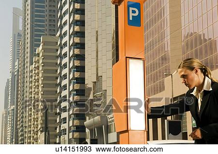 Stock Image - A businesswoman using a parking meter. Fotosearch
