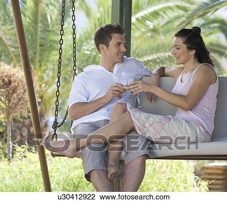 Stock Image - A couple drinking wine on a swing. Fotosearch