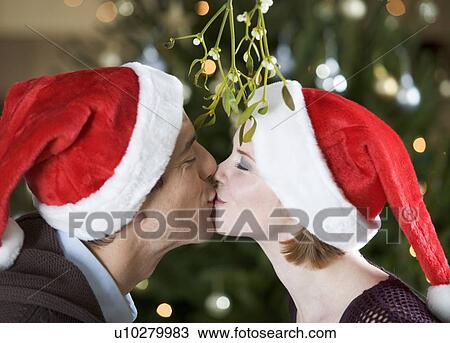 Stock Image - A couple kissing beneath the mistletoe. Fotosearch