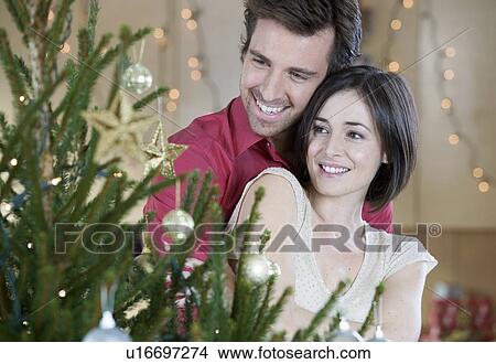 Picture - A couple standing by the Christmas tree. Fotosearch