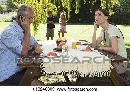 Stock Photo - A father receiving a business call during a family lunch in the garden. Fotosearch