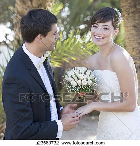 A groom placing the ring on his bride View Large Photo Image Stock Image - A groom placing the ring on his bride. Fotosearch