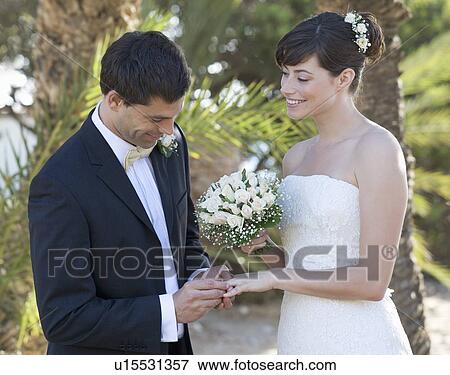 Stock Photo - A groom placing the ring on his bride. Fotosearch