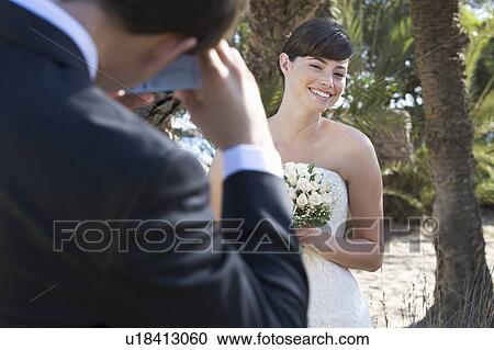 Stock Image - A groom taking a photograph of his bride. Fotosearch