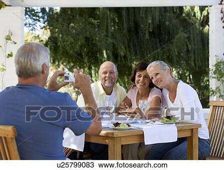 Stock Image - A group of senior couples at a restaurant, man taking picture with digital camera. Fotosearch