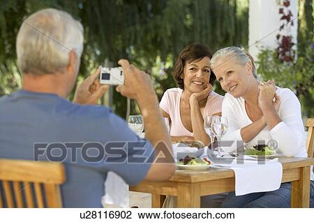 A group of senior couples at a restaurant, man taking picture with digital camera View Large Photo Image Stock Image - A group of senior couples at a restaurant, man taking picture with digital camera. Fotosearch