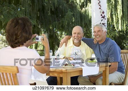 Stock Photo - A group of senior couples at a restaurant, woman taking picture with digital camera. Fotosearch