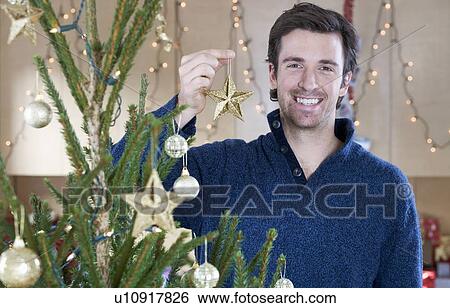 Stock Photograph - A man decorating the Christmas tree. Fotosearch