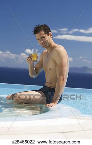 Stock Image - A man drinking fruit juice by a pool. Fotosearch