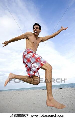 Stock Photo - A man in shorts jumping on a beach. Fotosearch