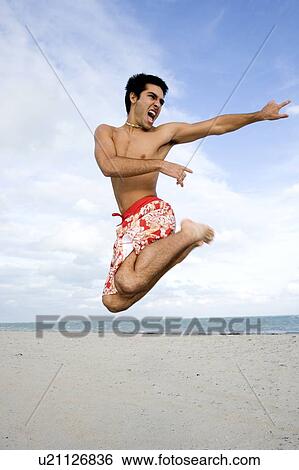 Stock Photograph - A man in shorts jumping on a beach. Fotosearch