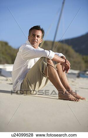 Stock Photo - A man sitting on a beach. Fotosearch