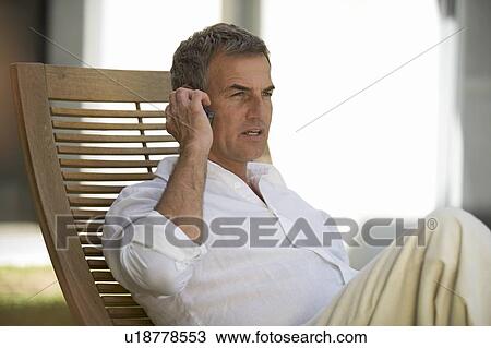 Stock Image - A man sitting on a sun lounger using a mobile phone. Fotosearch