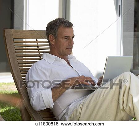 Stock Photograph - A man sitting on a sun lounger using a laptop. Fotosearch