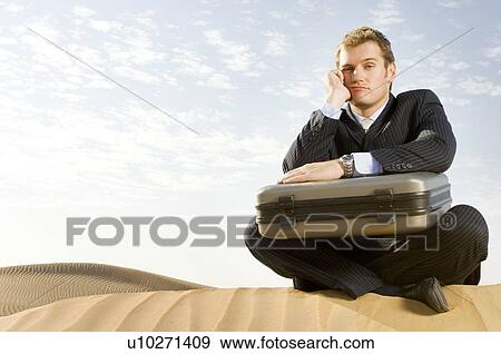 Stock Photo - A man with a suitcase sitting in a desert. Fotosearch