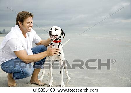 Stock Photo - A man with his dog on a beach. Fotosearch