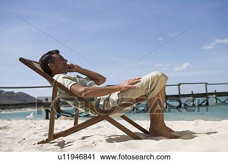 A mature man sitting in a deck chair on a cell phone View Large Photo Image Stock Image - A mature man sitting in a deck chair on a cell phone. Fotosearch