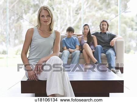 A mother sitting on a coffee table with her family sitting on a sofa View Large Photo Image Picture - A mother sitting on a coffee table with her family sitting on a sofa. Fotosearch