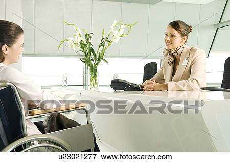 Stock Photo - A receptionist greeting a woman in a wheelchair. Fotosearch