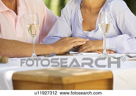 Stock Image - A senior couple celebrating close-up of hands and champagne flutes. Fotosearch