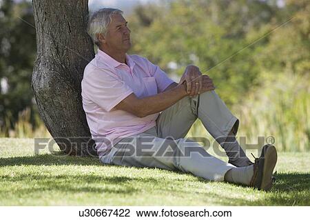 A senior man sitting under a tree View Large Photo Image Stock Image - A senior man sitting under a tree. Fotosearch