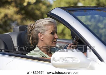 A senior woman driving a car whilst on a cell phone View Large Photo Image Picture - A senior woman driving a car whilst on a cell phone. Fotosearch