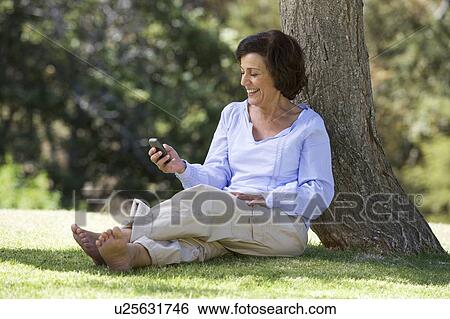 A senior woman sitting under a tree using a mobile telephone View Large Photo Image Stock Photograph - A senior woman sitting under a tree using a mobile telephone. Fotosearch