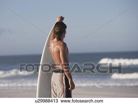 A surfer standing on a beach View Large Photo Image Stock Image - A surfer standing on a beach. Fotosearch