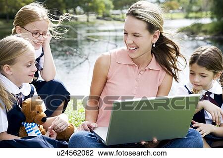 Stock Image - A teacher and children using a laptop outside. Fotosearch