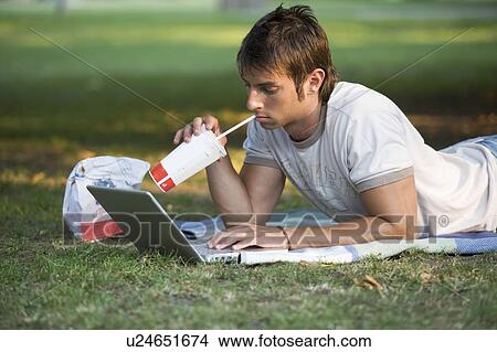 Picture - A teenage boy working on a laptop in a park. Fotosearch