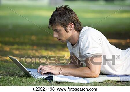 A teenage boy working on a laptop in a park View Large Photo Image Stock Photo - A teenage boy working on a laptop in a park. Fotosearch