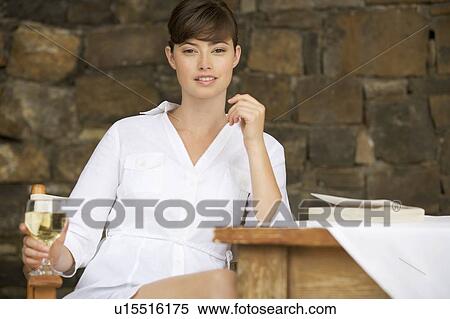 Stock Photography - A woman drinking a glass of wine sitting at a table. Fotosearch